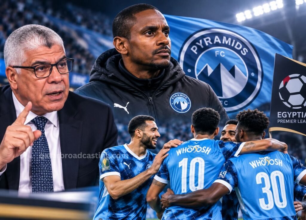 qatarbroadcastingcom 5 - Qatar Broadcasting Coach speaks to players in blue soccer jerseys on a stadium field with a team crest banner in the background, gesturing with his finger raised in emphasis.